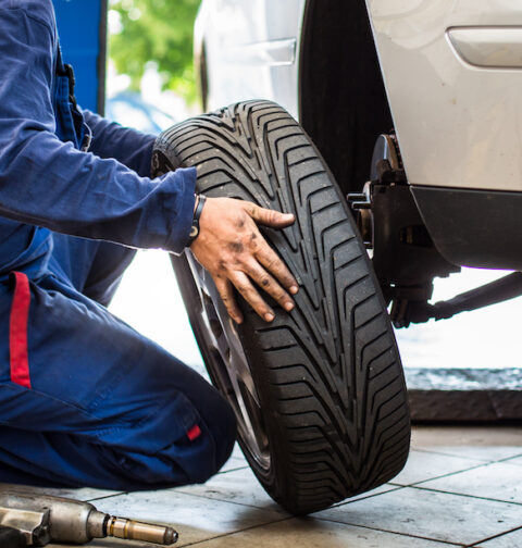Auto rataste juures töötav mehaanik kevadpäikeses rehve vahetamas