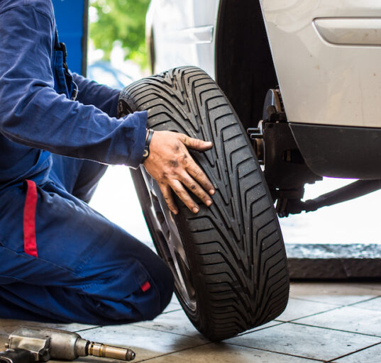 Auto rataste juures töötav mehaanik kevadpäikeses rehve vahetamas