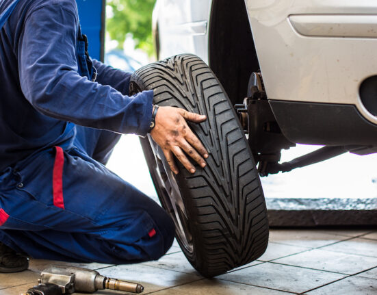 Auto rataste juures töötav mehaanik kevadpäikeses rehve vahetamas