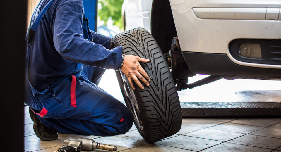 Auto rataste juures töötav mehaanik kevadpäikeses rehve vahetamas