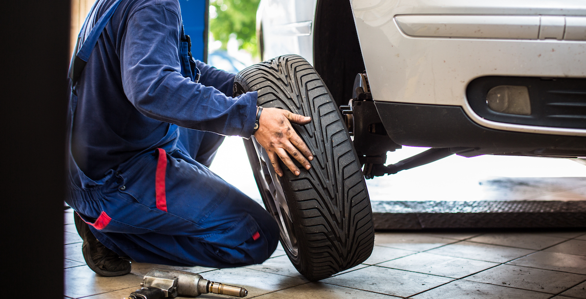 Auto rataste juures töötav mehaanik kevadpäikeses rehve vahetamas